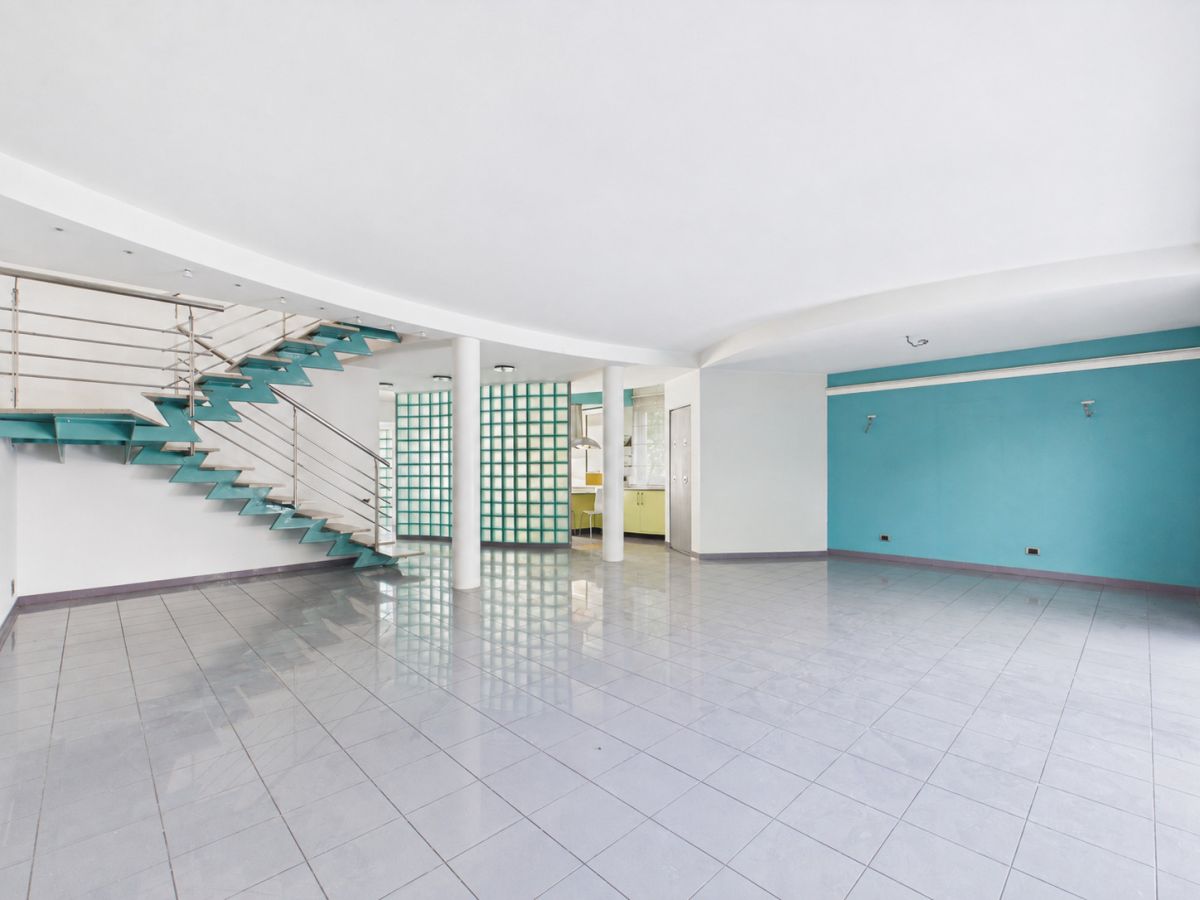 Empty modern interior with a teal zigzag staircase along the left wall, glass block wall, and turquoise accent wall.