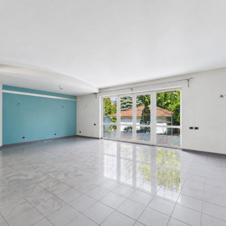 Empty modern living room with white walls, a blue accent wall, and large glass doors opening to a garden area