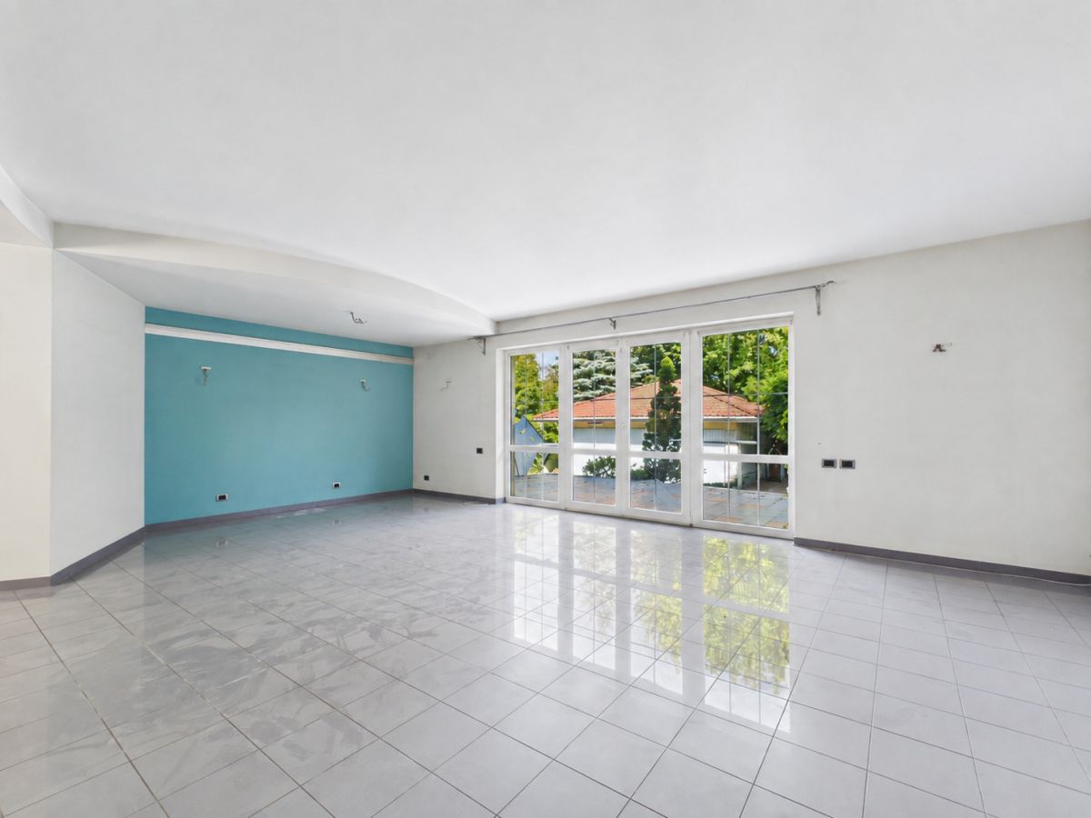Empty modern living room with white walls, a blue accent wall, and large glass doors opening to a garden area
