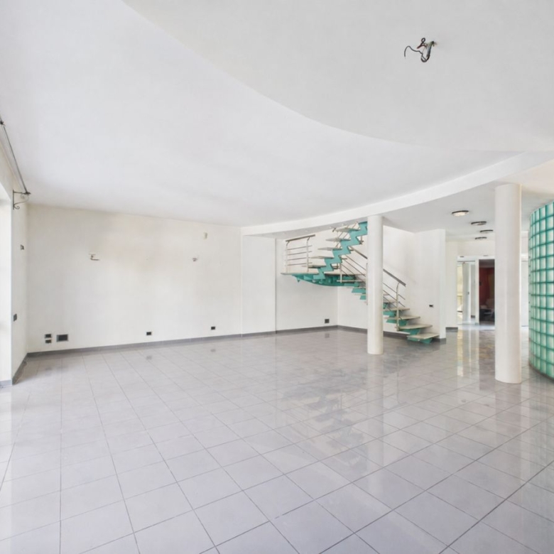 Spacious white lobby with large glass doors, glossy tiled floor, and a turquoise curved staircase.