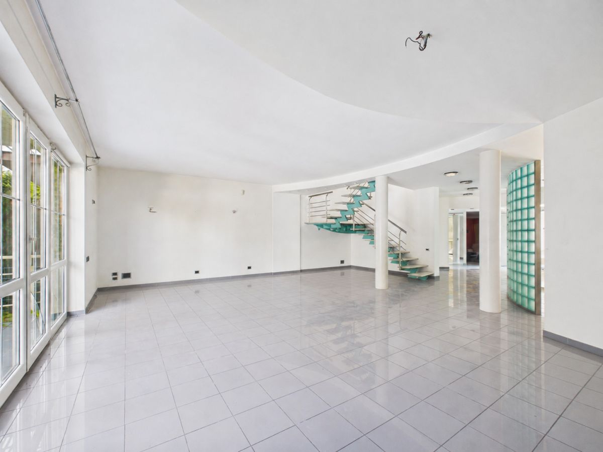 Spacious white lobby with large glass doors, glossy tiled floor, and a turquoise curved staircase.