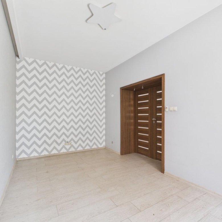 Empty room with a chevron-patterned accent wall, light gray walls, and a wooden door with horizontal slats.