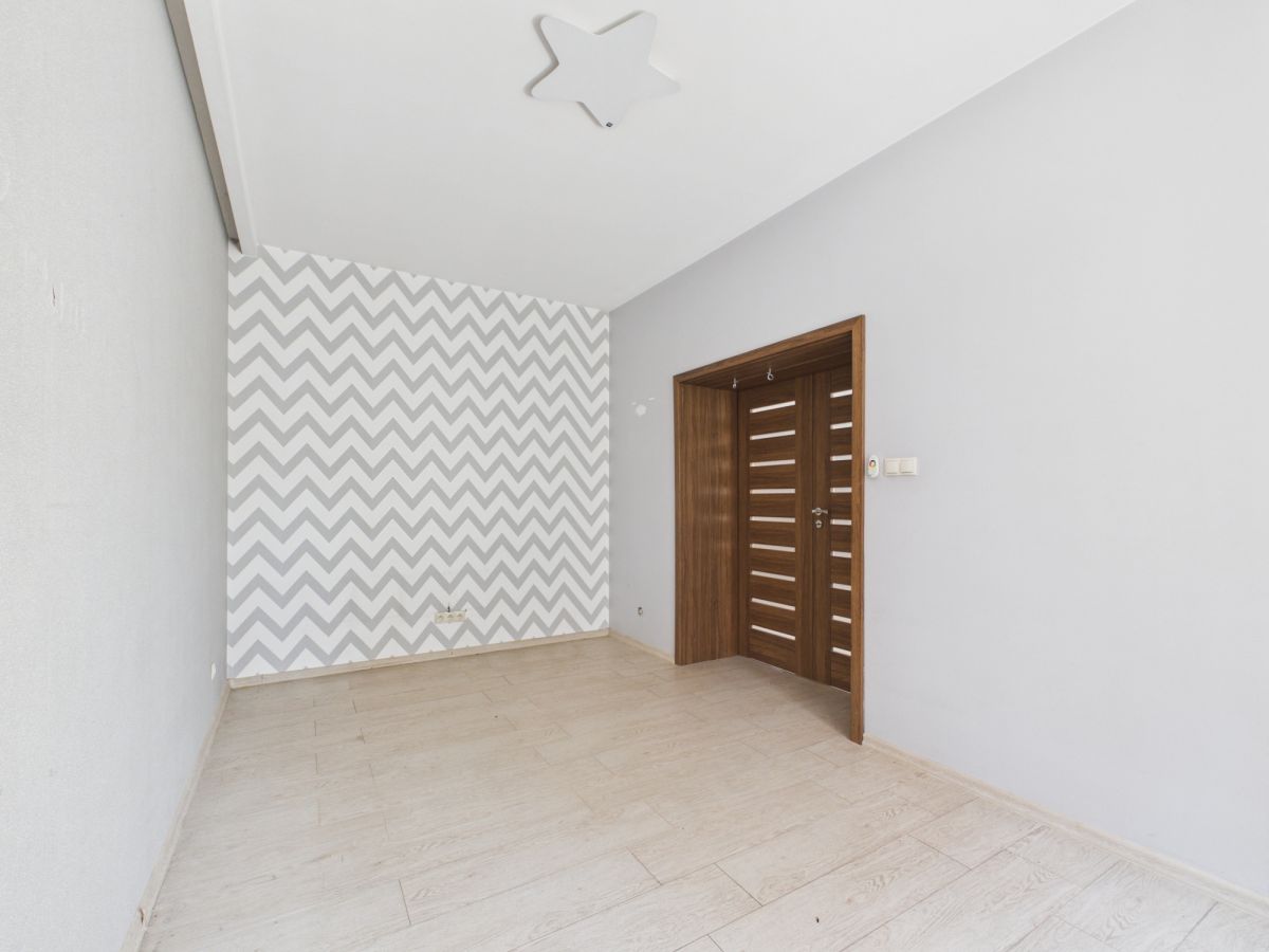 Empty room with a chevron-patterned accent wall, light gray walls, and a wooden door with horizontal slats.