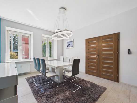 Modern dining room with a white rectangular table, white/blue chairs, a sculptural circular chandelier, and wooden double doors.
