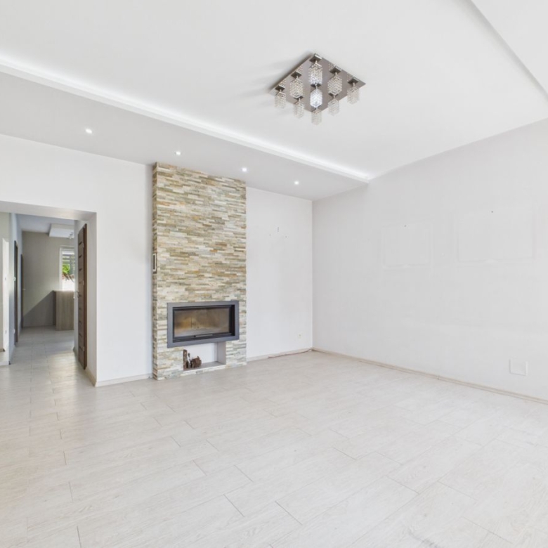Bright empty living room with a stone-clad fireplace wall and built-in gas fire, white walls, and light tile flooring.