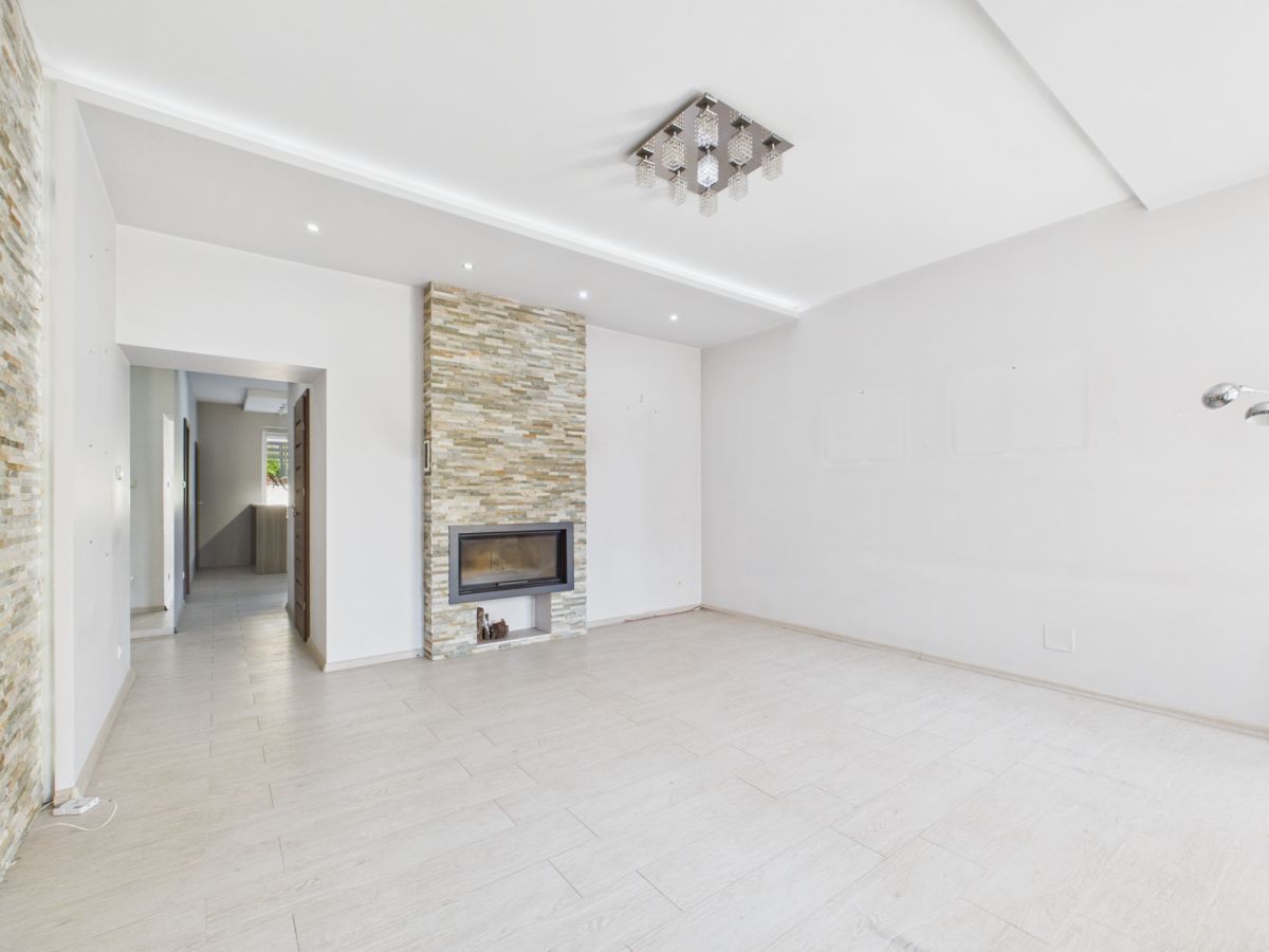 Bright empty living room with a stone-clad fireplace wall and built-in gas fire, white walls, and light tile flooring.