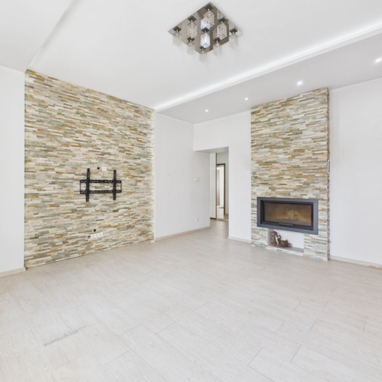 Bright living room with two stone accent walls, a wall-mounted TV bracket, and a built-in fireplace, empty and ready for furnishings.