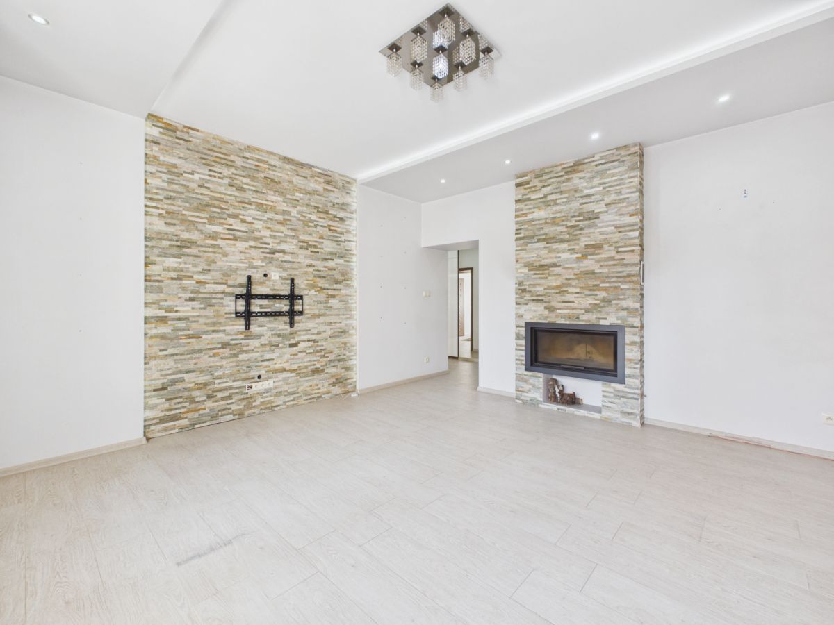 Bright living room with two stone accent walls, a wall-mounted TV bracket, and a built-in fireplace, empty and ready for furnishings.
