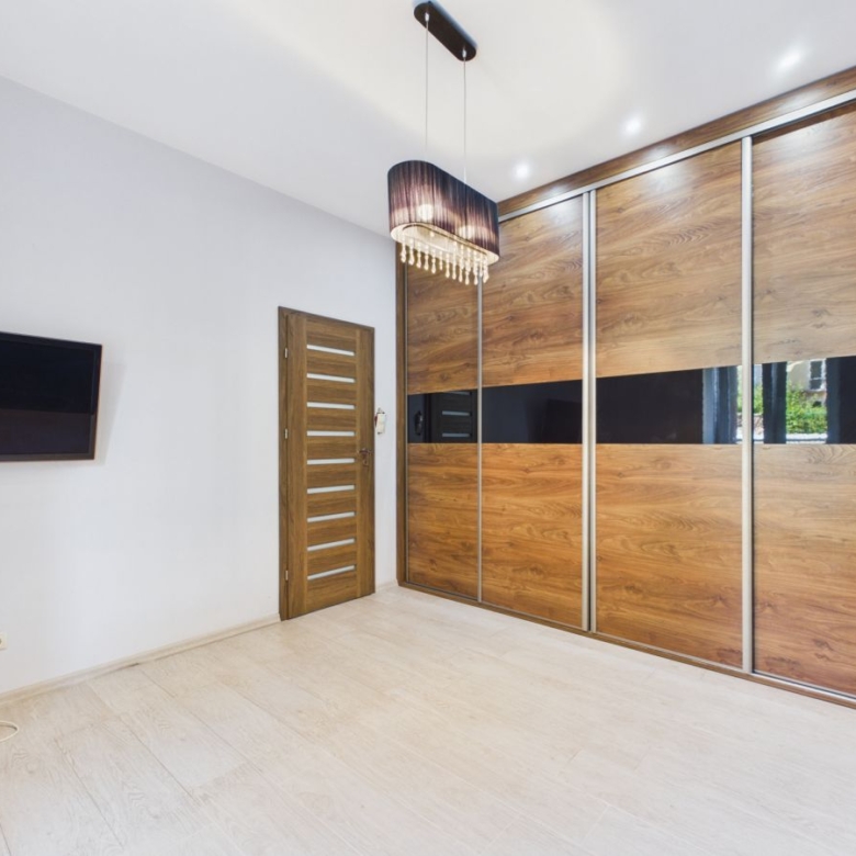 Minimalist bedroom with a large wooden sliding closet, a door, and a wall-mounted TV on a white wall