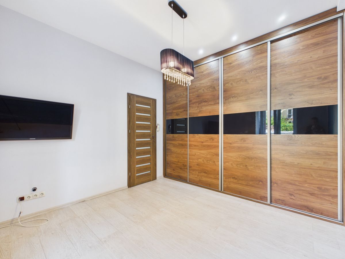 Minimalist bedroom with a large wooden sliding closet, a door, and a wall-mounted TV on a white wall