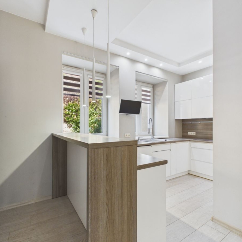 Bright modern kitchen with white cabinets and an oak-toned island, underpendant lights, and large windows overlooking greenery.