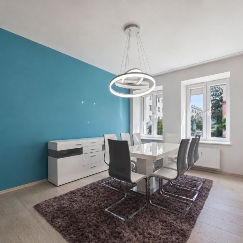 Modern dining room with teal accent wall, white table and six chairs on a brown shag rug.