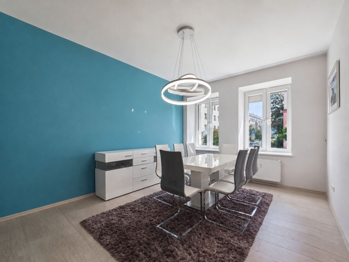 Modern dining room with teal accent wall, white table and six chairs on a brown shag rug.