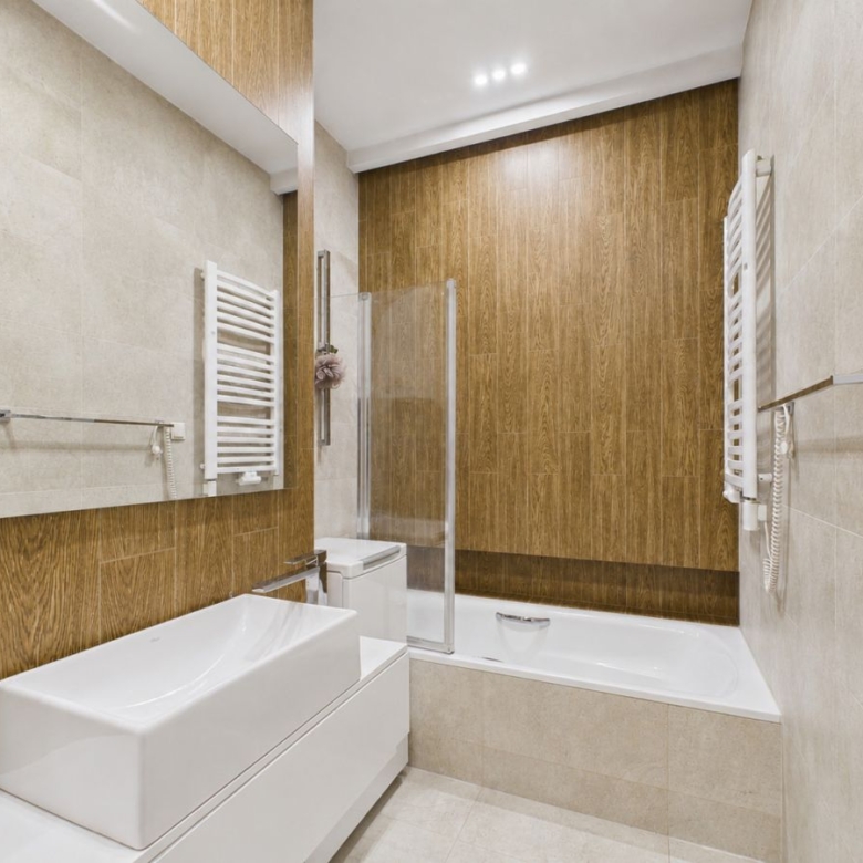 Modern white bathroom with a wood-paneled accent wall, wall-mounted sink, and bathtub with a glass shower screen.