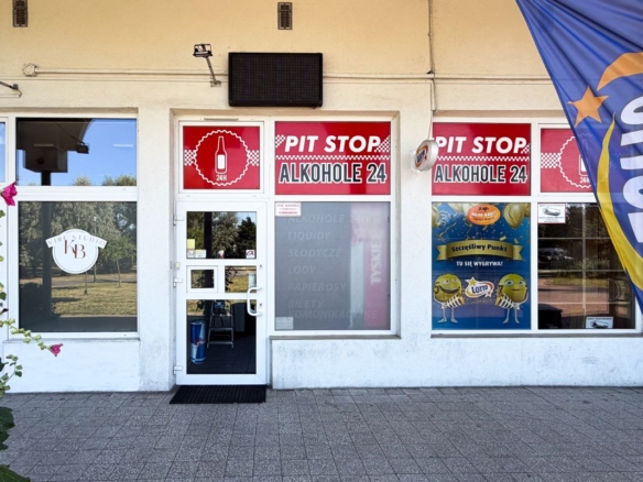 Storefront with red Pit Stop Alkohol 24 signs, glass door, and windows; a blue flag is on the right.