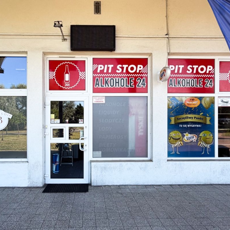 Storefront with red Pit Stop Alkohol 24 signs, glass door, and windows; a blue flag is on the right.