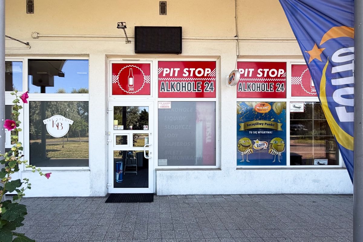 Storefront with red Pit Stop Alkohol 24 signs, glass door, and windows; a blue flag is on the right.