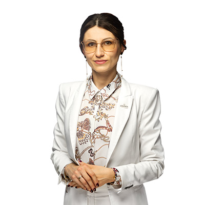 Professional woman in a white blazer and floral blouse, wearing glasses, with hands clasped in front against a white background.